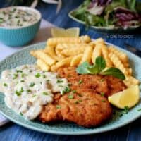 Chicken schnitzel with mushroom sauce served with french fries and lemon wedge.