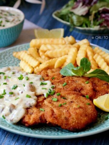 Chicken schnitzel with mushroom sauce served with french fries and lemon wedge.