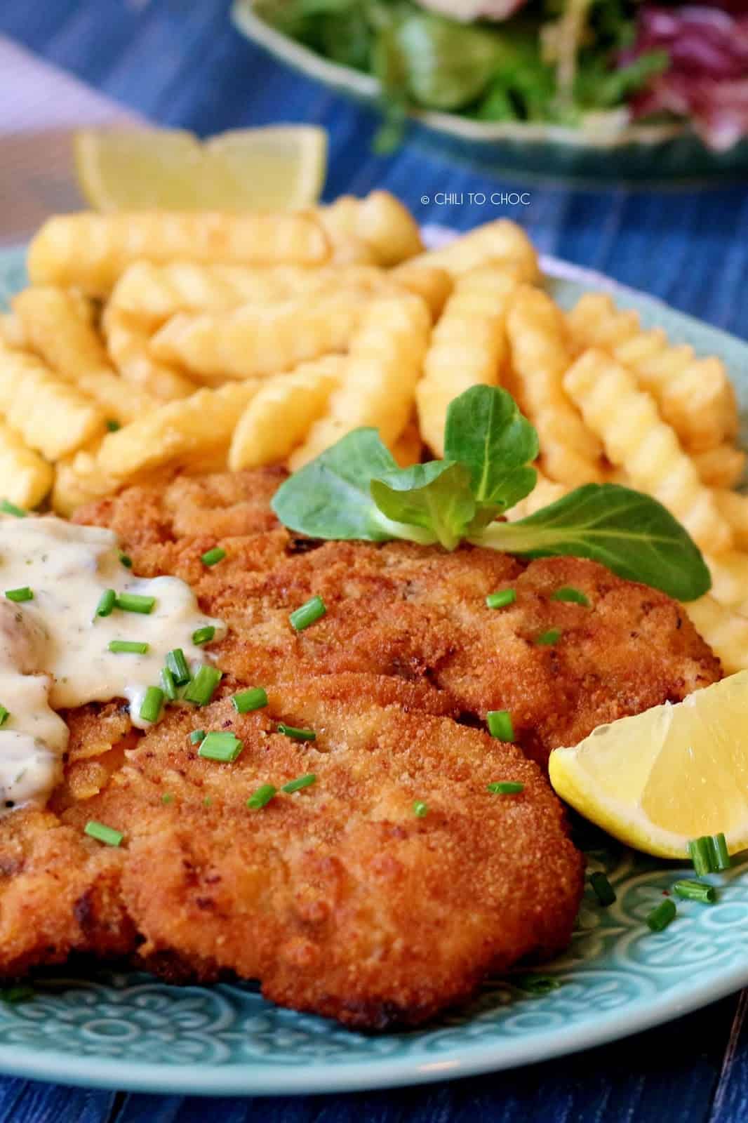 Crispy chicken schnitzel topped with chives and served with fries on a plate.