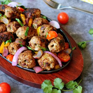 Gola kabab on a sizzling plate with cherry tomatoes, red onions and chopped coriander