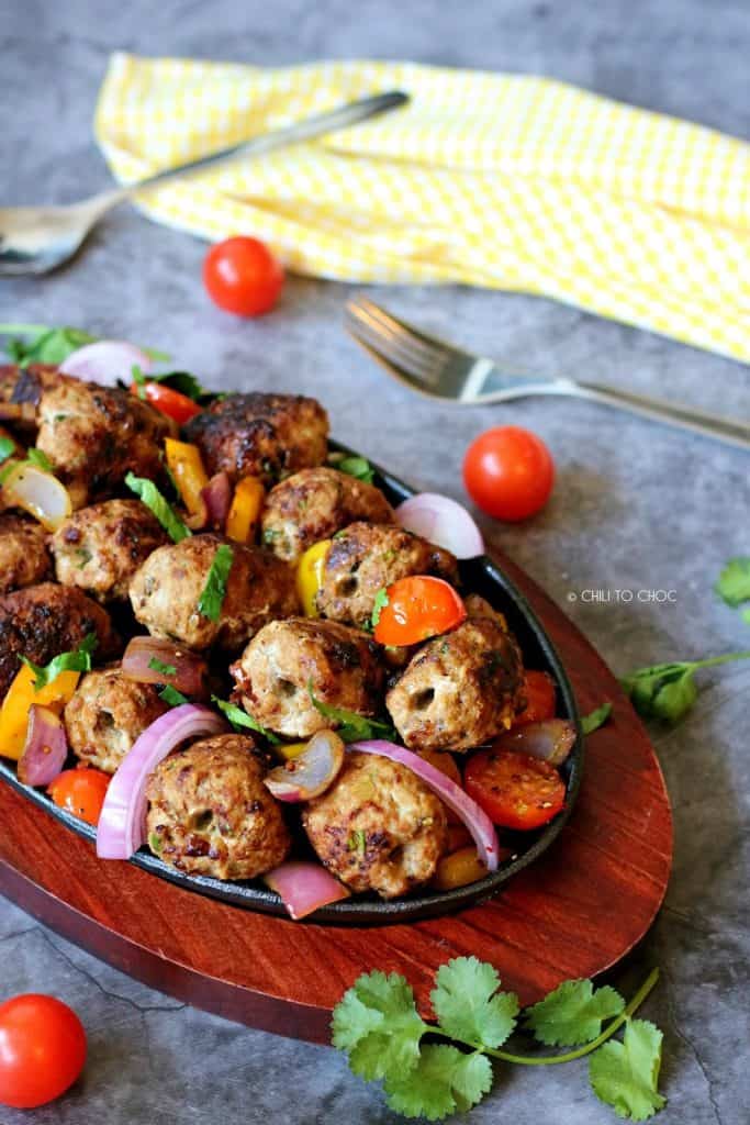 Pakistani gola kabab on grill plate garnished with red onions, cherry tomatoes and coriander