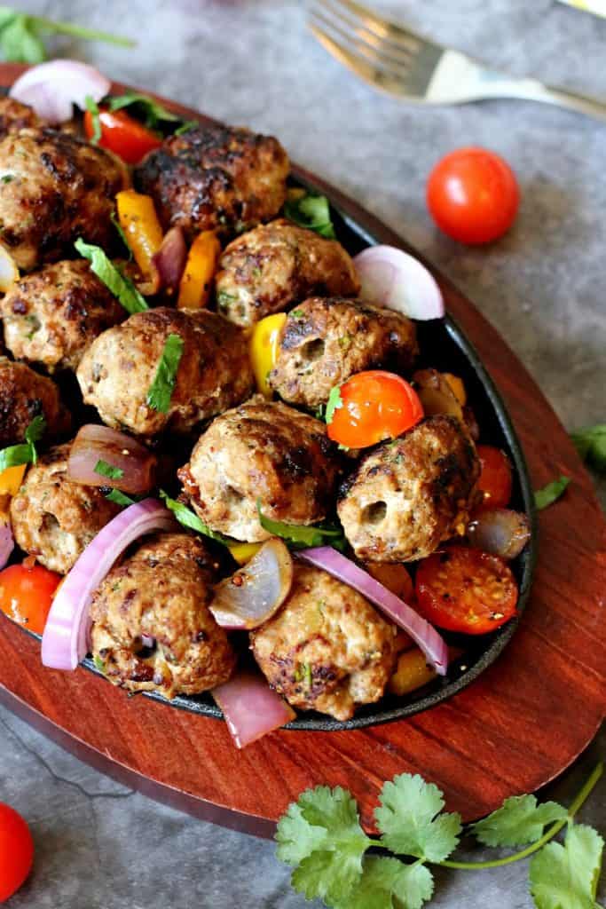 Closeup of gola kabab topped with chopped coriander, red onion slices and halved cherry tomatoes