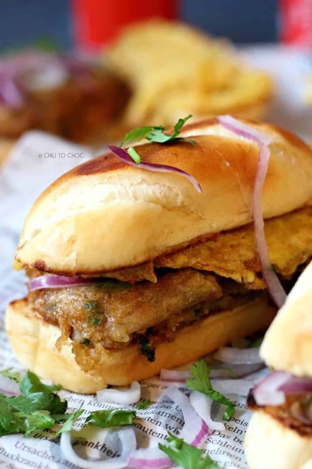 A vegetarian sandwich on a newspaper garnished with red onions and coriander