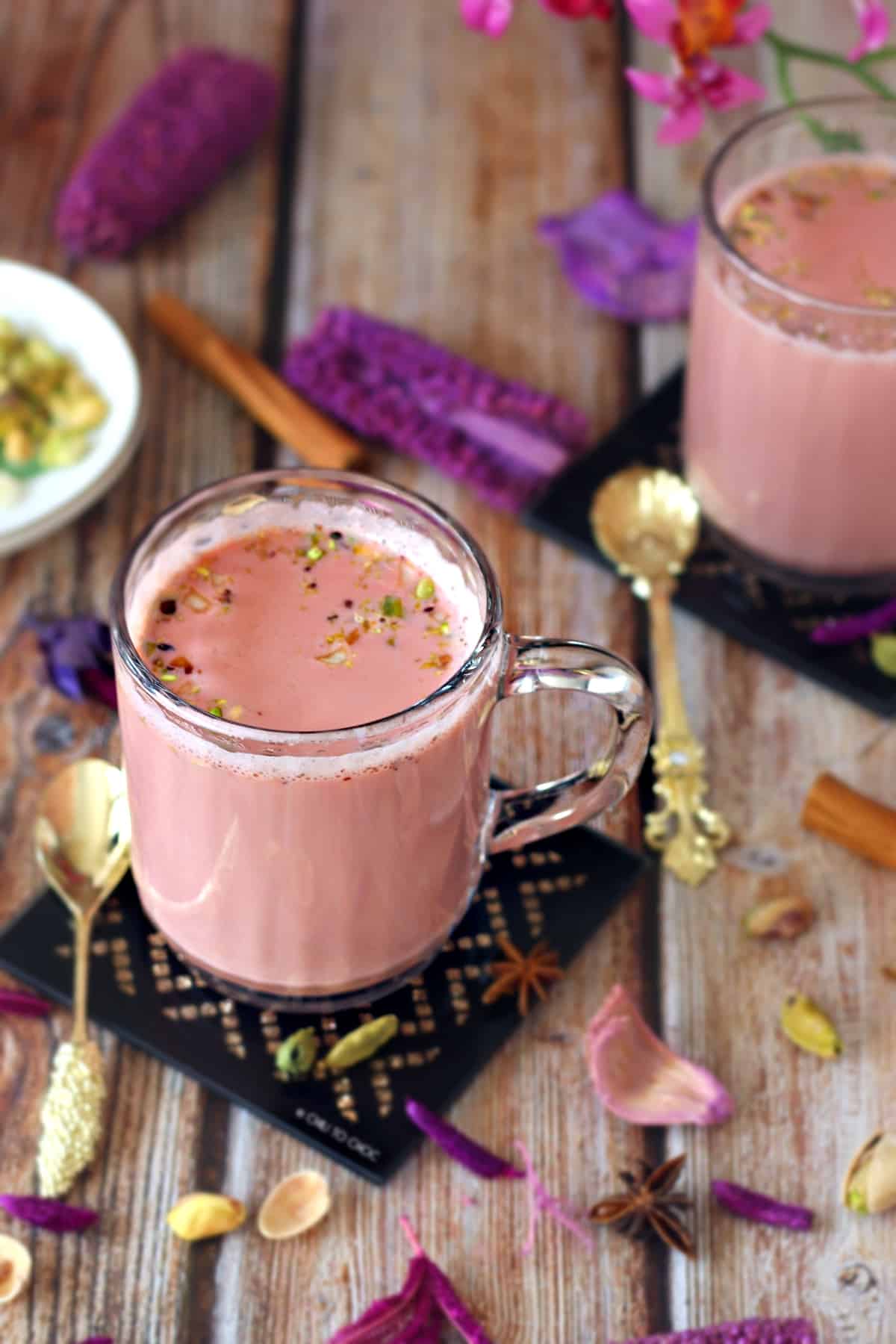 Pink milk tea in a clear mug on a black coaster garnished with sliced pistachios and almonds