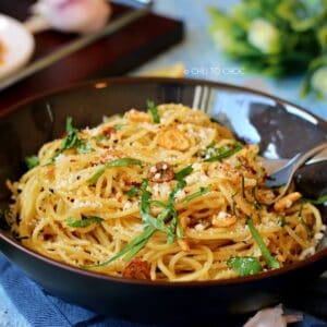 Spaghetti Aglio E Olio in a deep dish garnished with fried garlic, red chili flakes and Parmesan cheese
