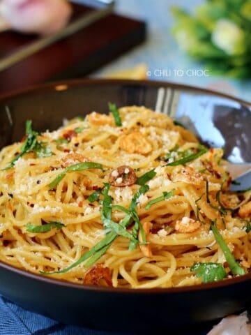 Spaghetti Aglio E Olio in a deep dish garnished with fried garlic, red chili flakes and Parmesan cheese