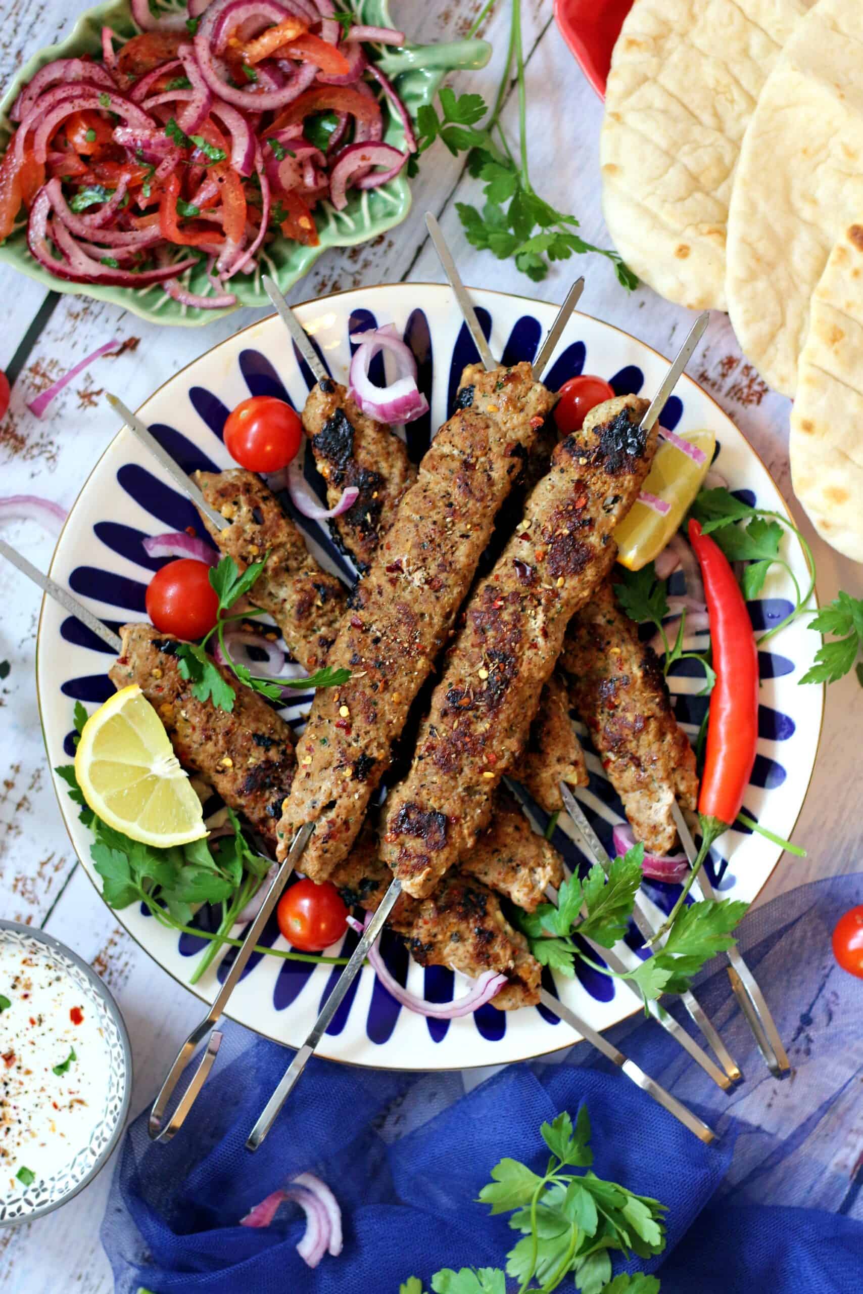 A plate of adana kebabs on skewers with garnish on top and sides around it