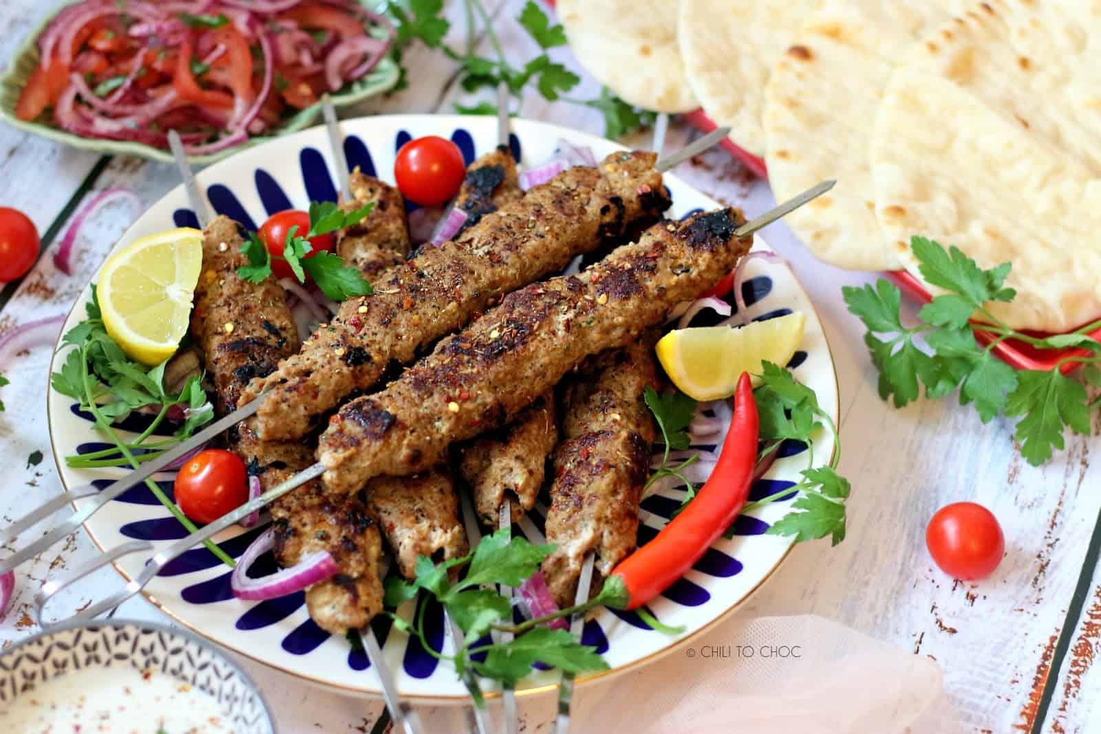 Adana Kebab with garnishes on top and Turkish salad and flatbread on the side