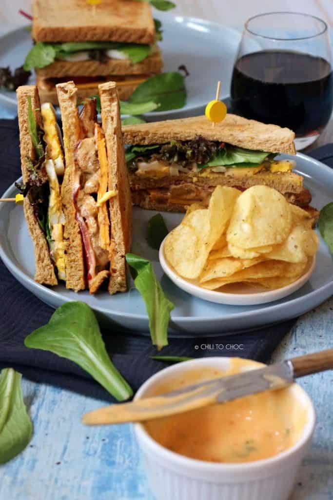 chicken club sandwich cut into triangles with a side of crisps on the plate