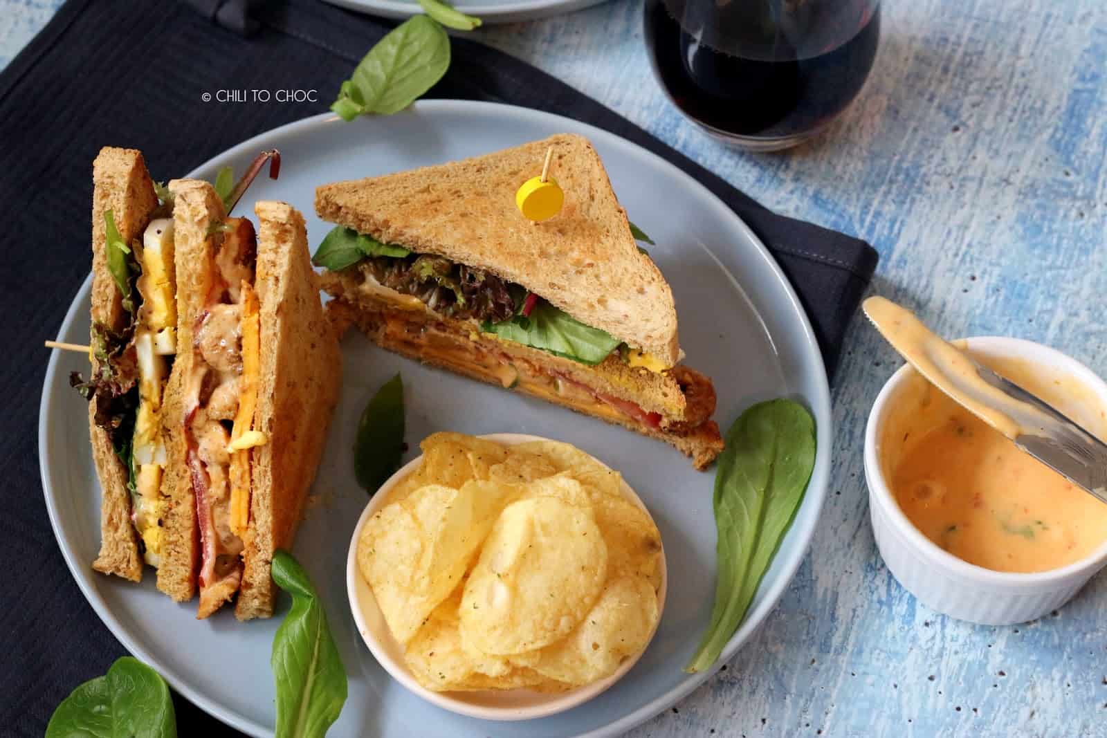 two triangles of club sandwich on a plate with a side of chips and a dip