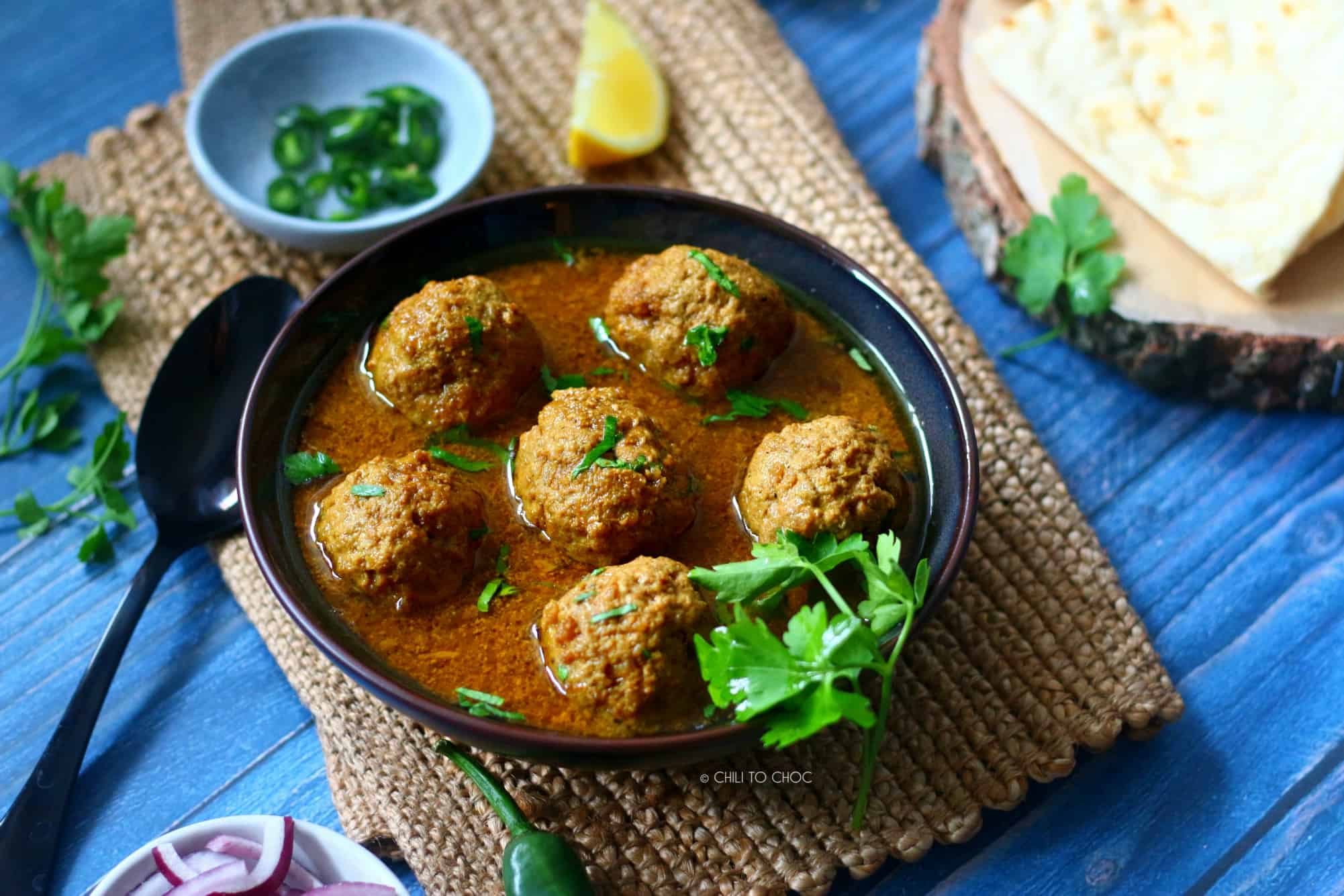 Beef Kofta Curry Pakistani Kofta Curry in bowl garnished with coriander and lemon and green chilies on the side