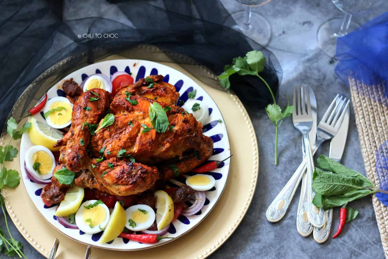 Murgh Musallam Whole chicken roast on a plate with cutlery on the side