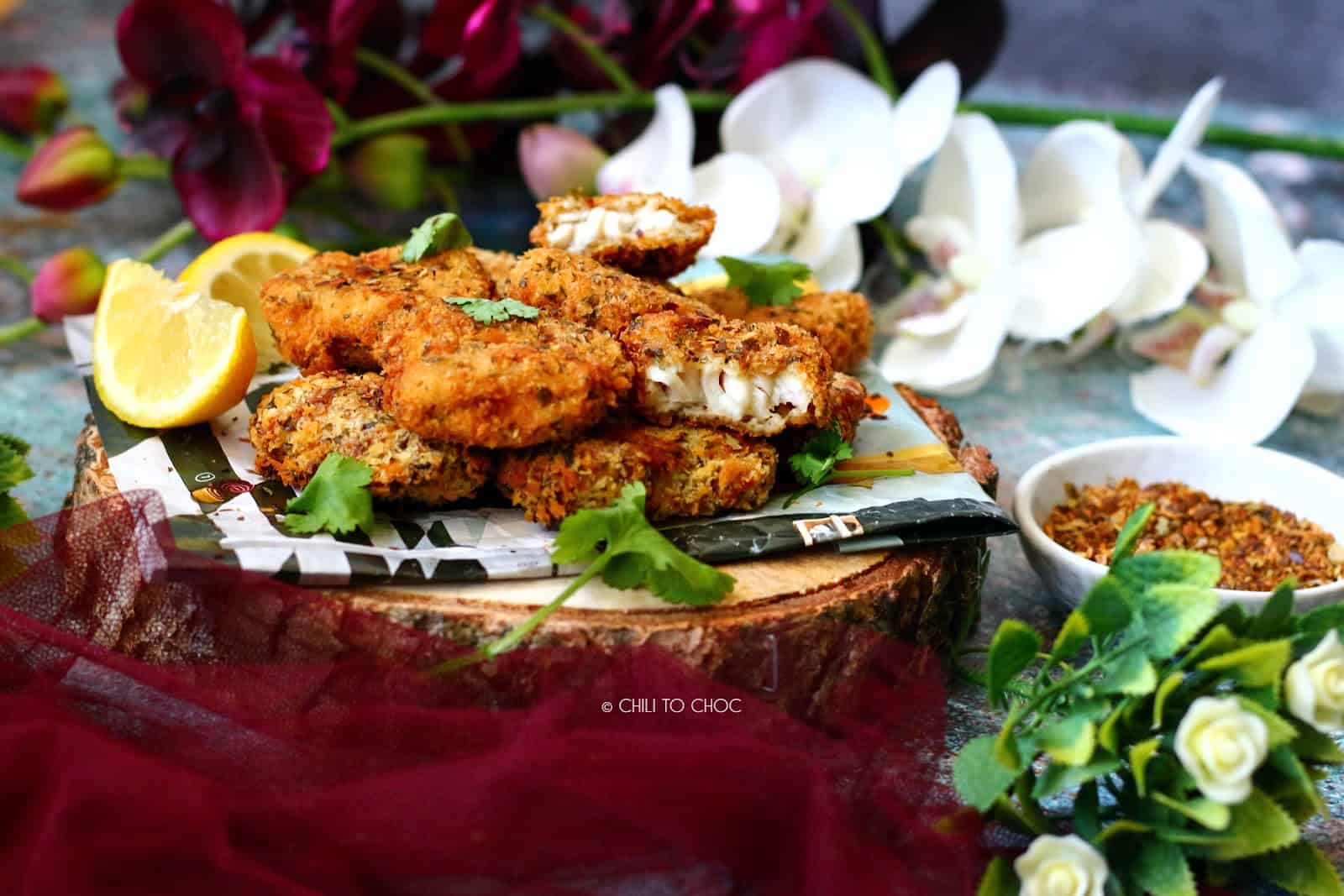 Crispy peri peri seasoned fish nuggets with lemon slices and chili flakes on the side