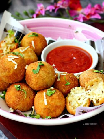 Potato and Cheese Balls on a pink shallow plate on a newspaper with ketchup on the side