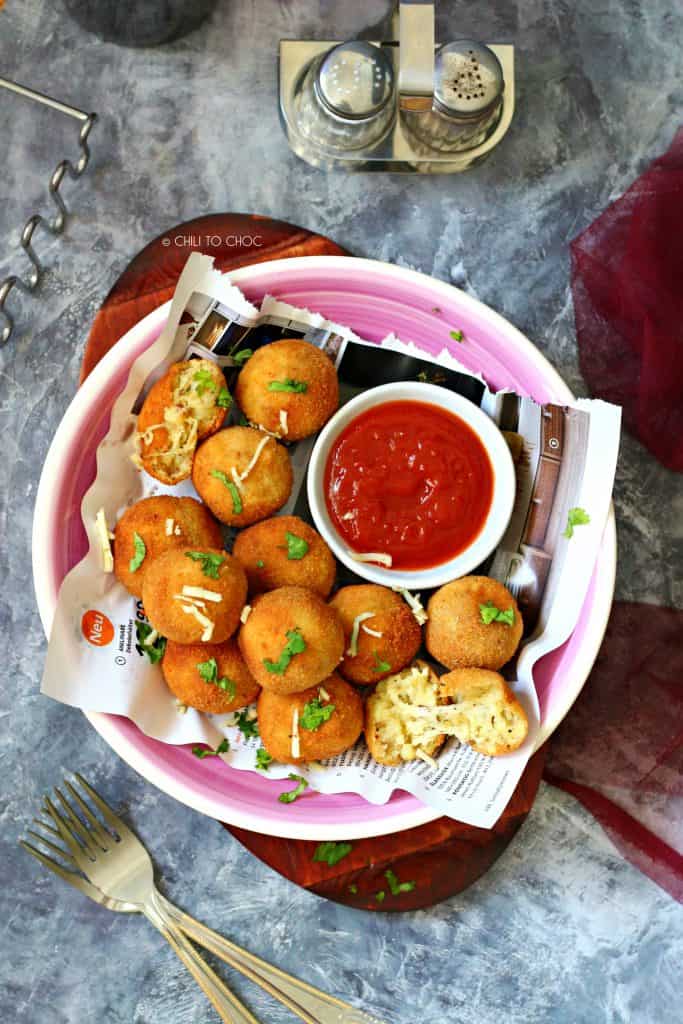 Mashed potato and cheese balls on a newspaper with ketchup on the side and salt and pepper shakers on top