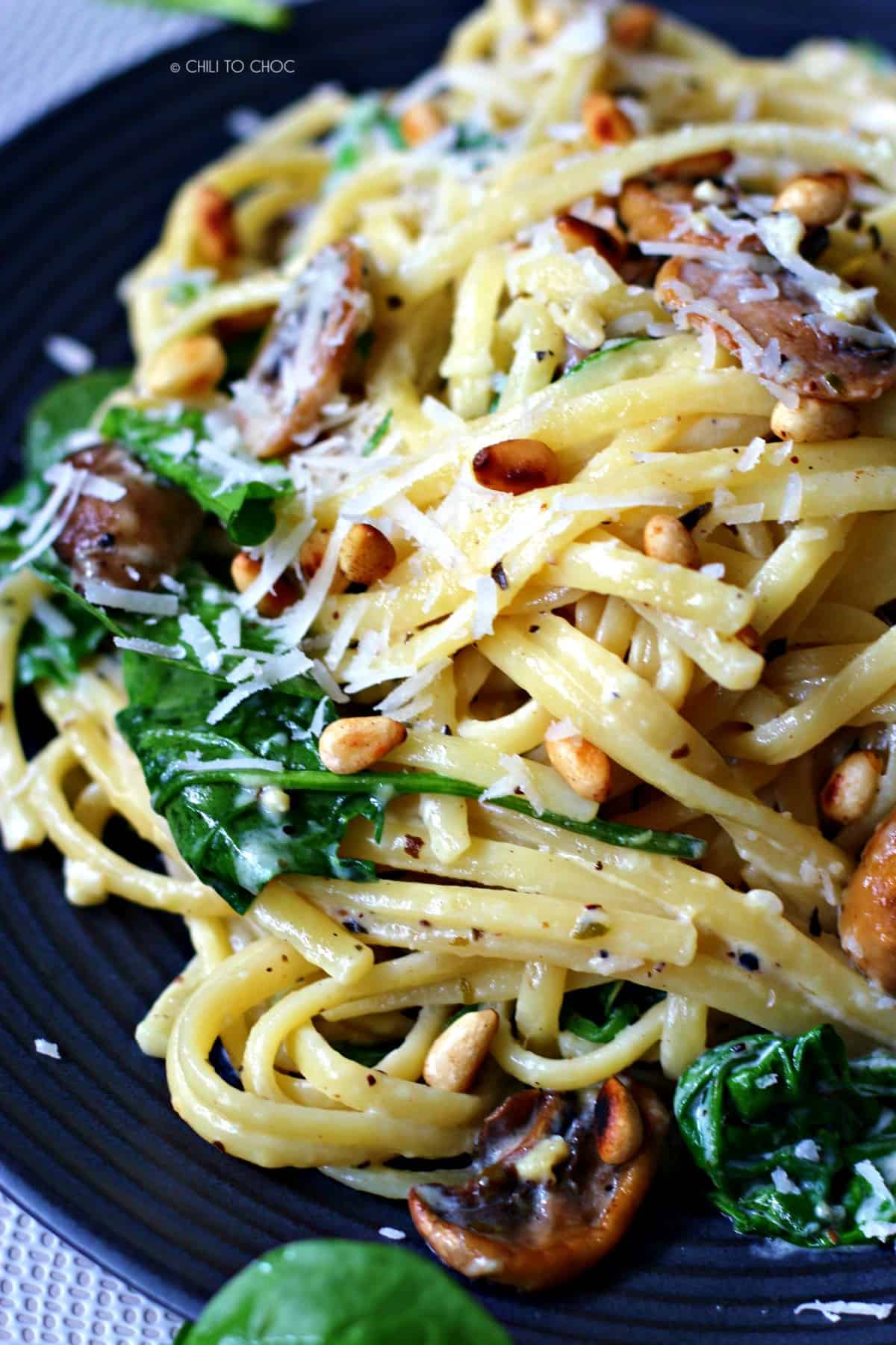 Creamy linguine pasta on a black dish with baby spinach, mushrooms and pine nuts