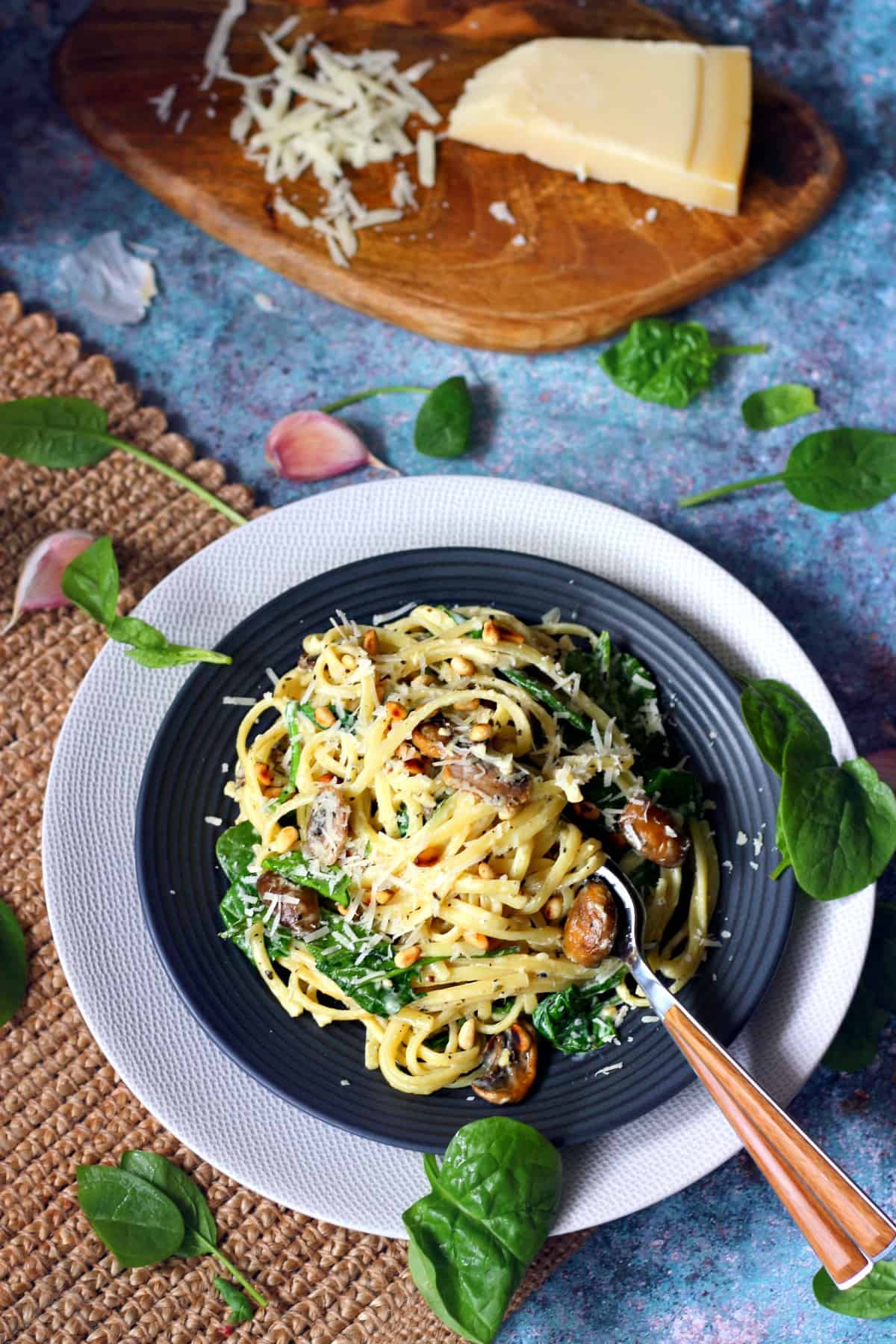 Creamy linguine pasta on a black dish with baby spinach, mushrooms and pine nuts