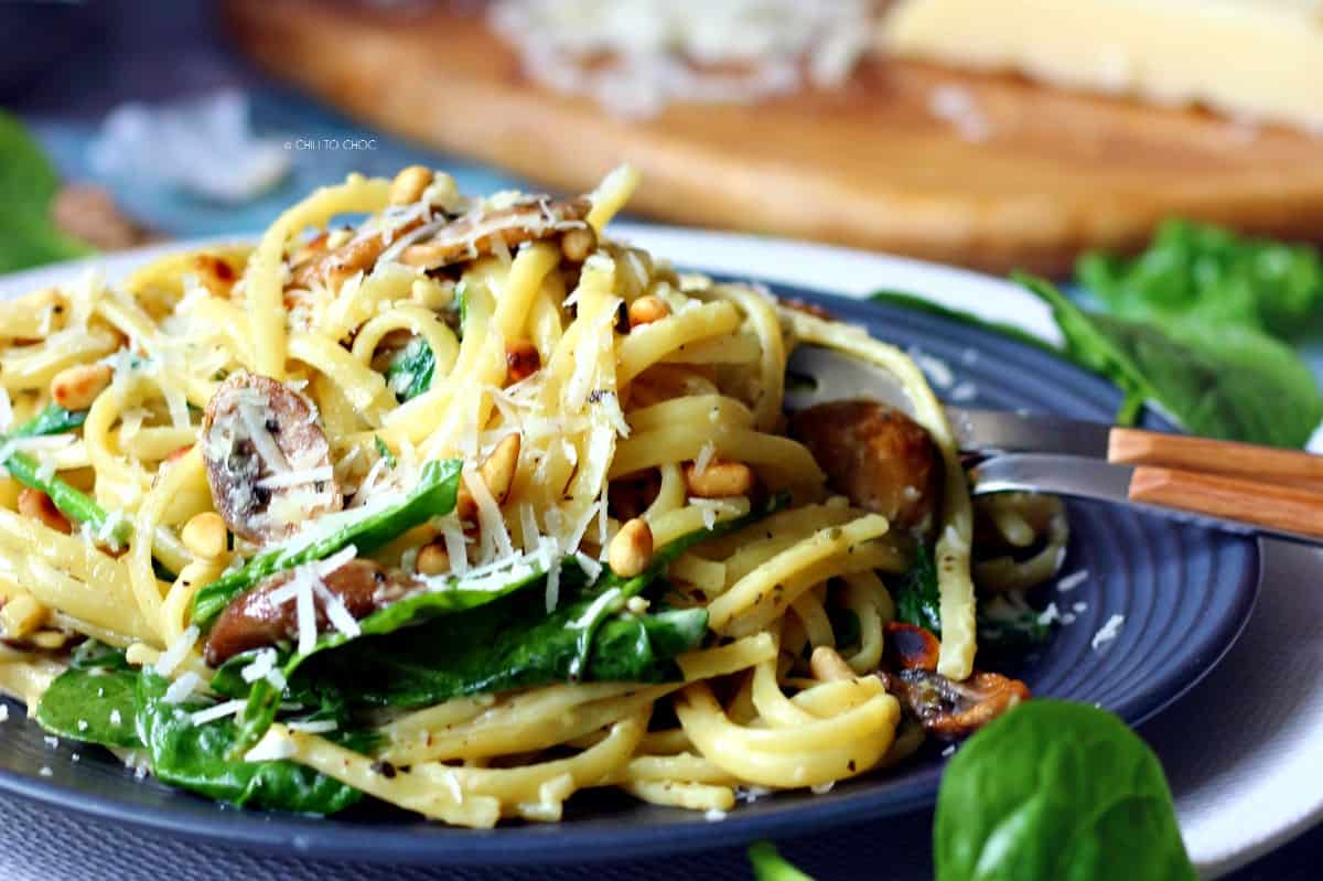 Creamy linguine pasta on a black dish with baby spinach, mushrooms and pine nuts