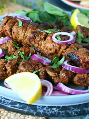 Bihari Kabab garnished with lemon wedges, red onion and fresh coriander