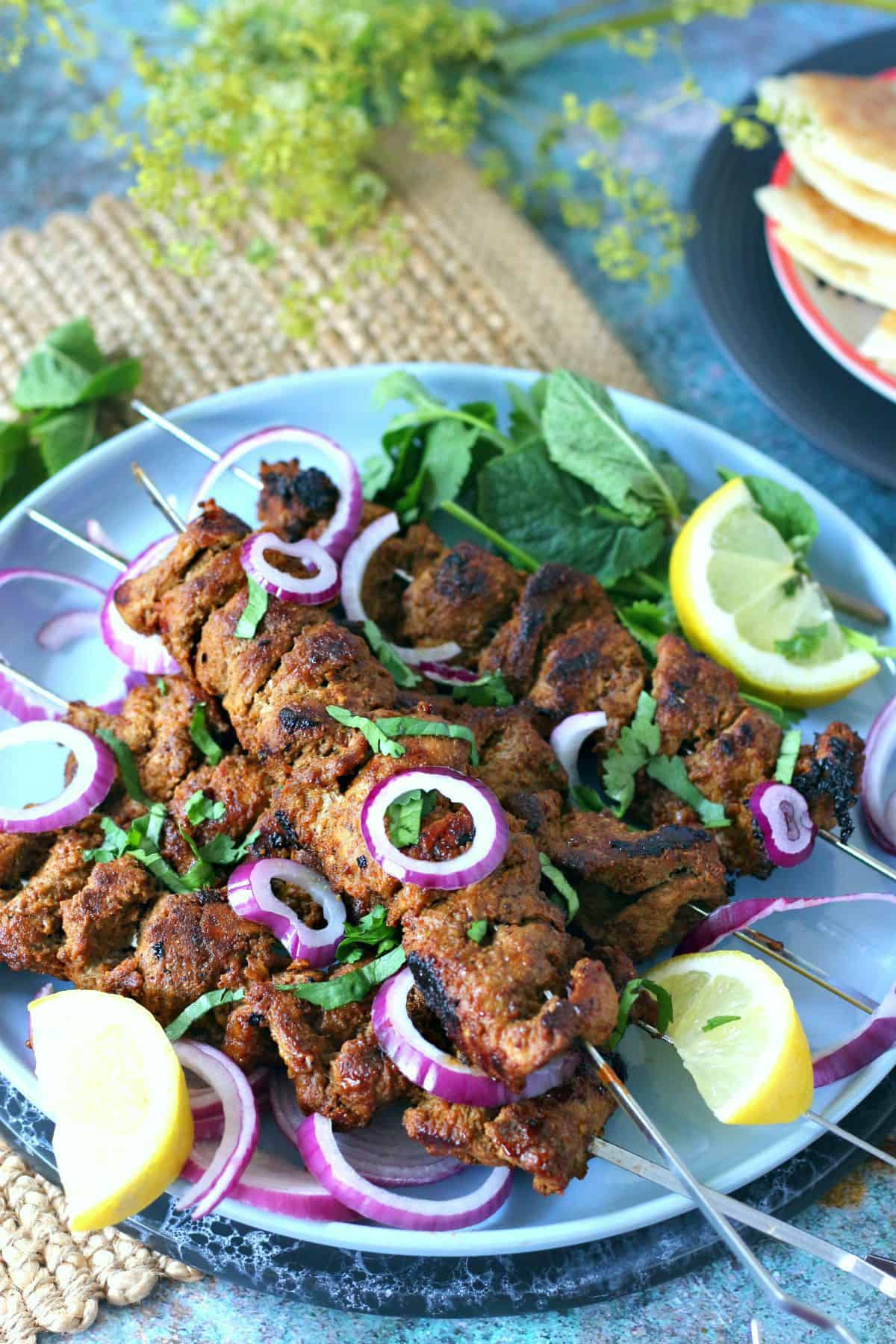 Bihari Kabab skewers garnished with lemon wedges, red onion and fresh coriander