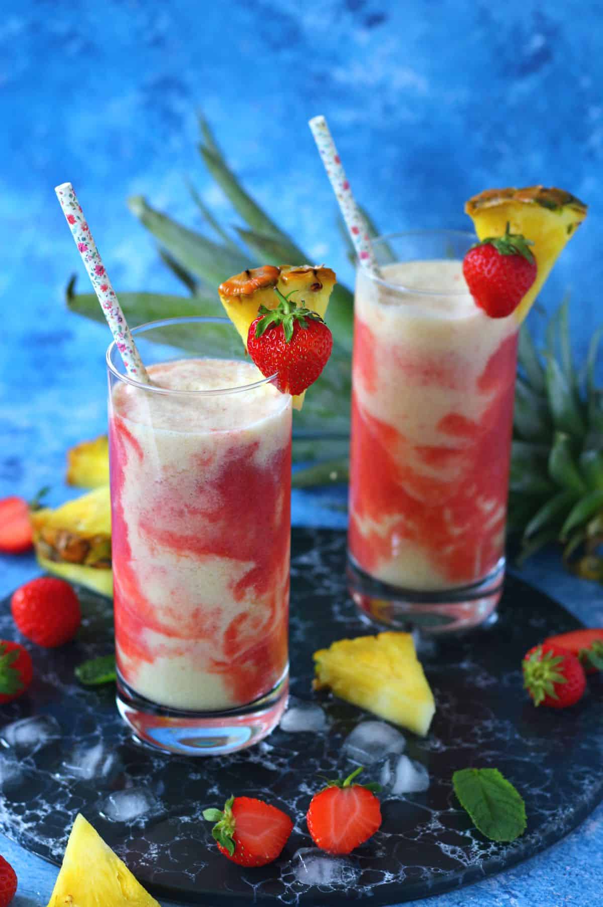 Two tall glasses of strawberry Pina Colada with straw and garnished with strawberry and pineapple wedge