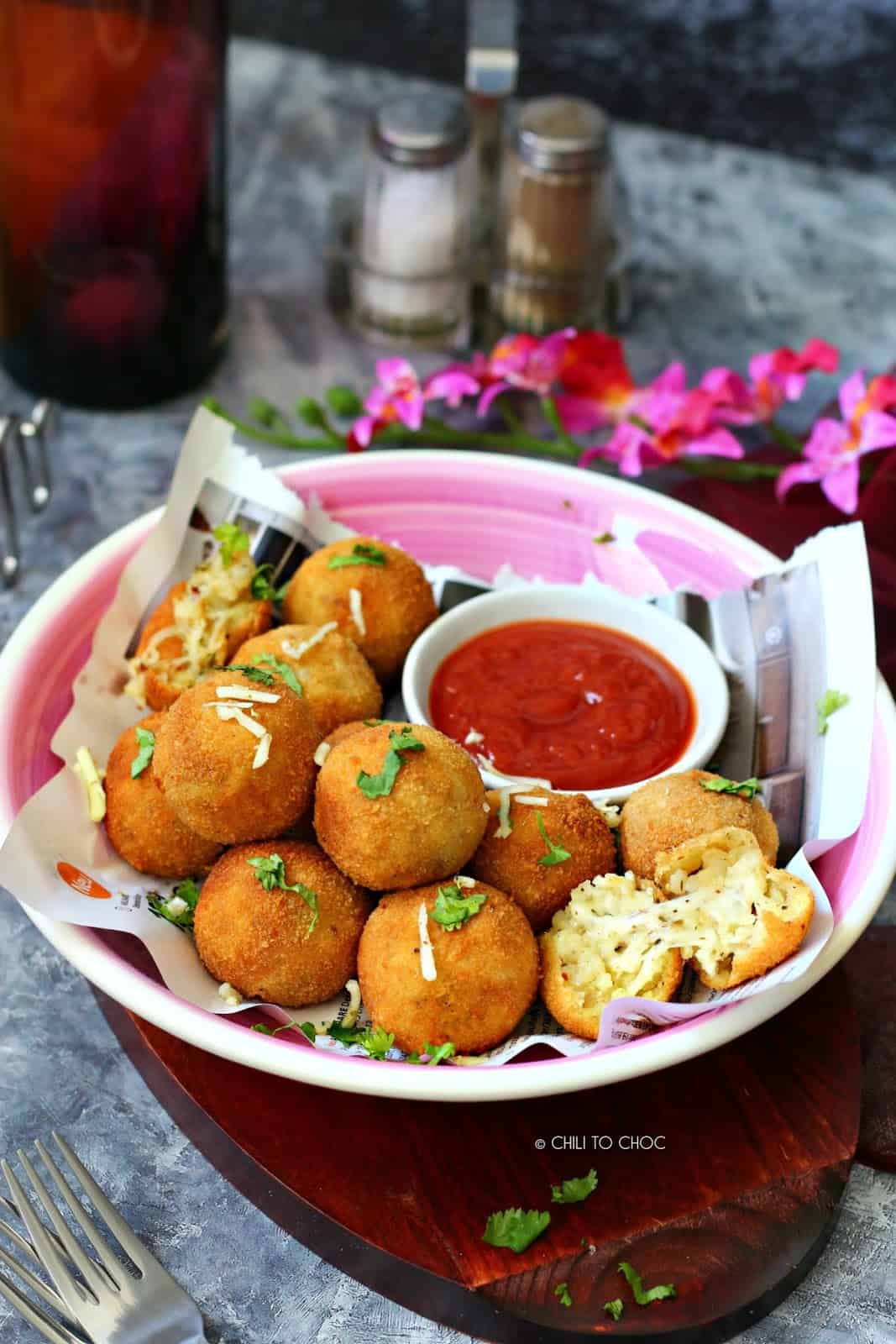 potato balls on a newspaper with a pink shallow dish underneath it and served with a side of ketchup