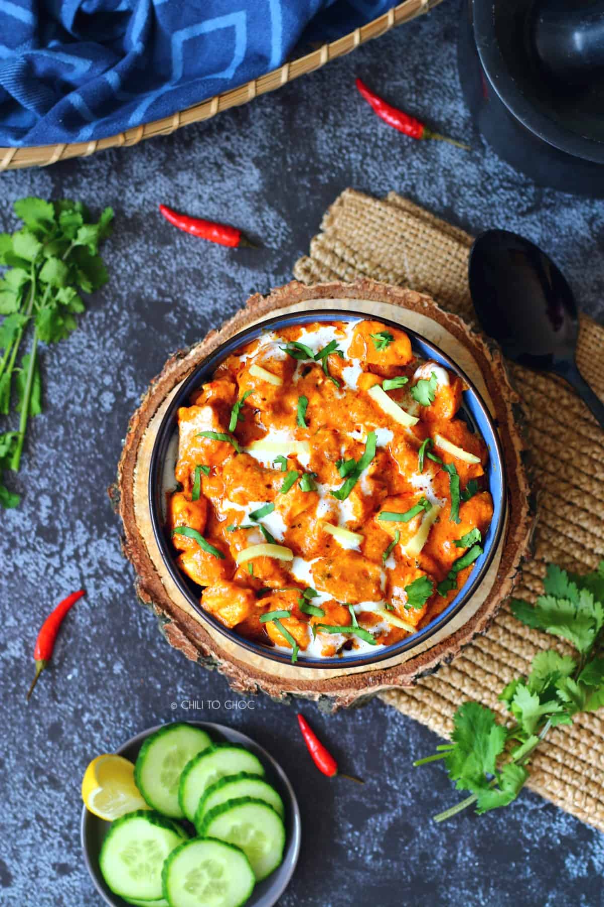 Chicken handi in a bowl with red chilies, cucumber slices and coriander on the side