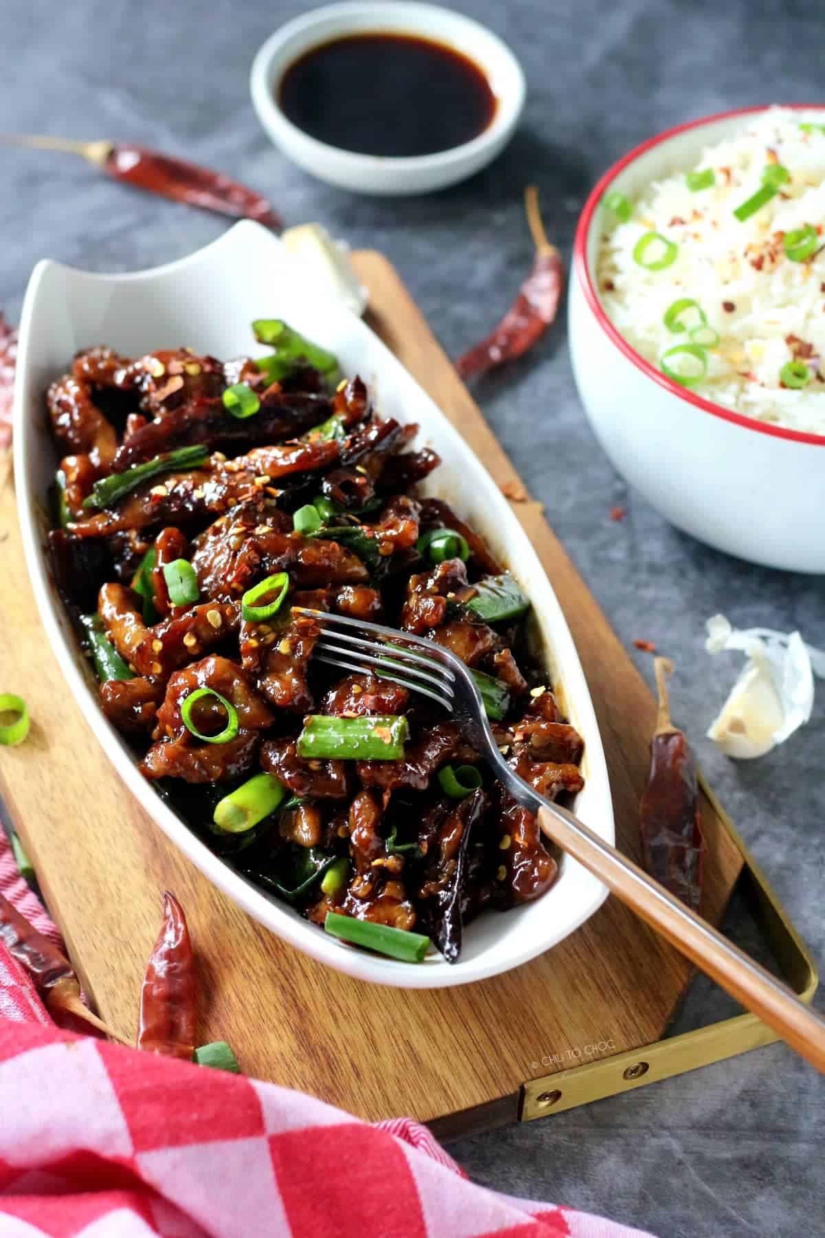 Spicy Mongolian Beef on a wooden tray topped with spring onion and dried red chilies around it