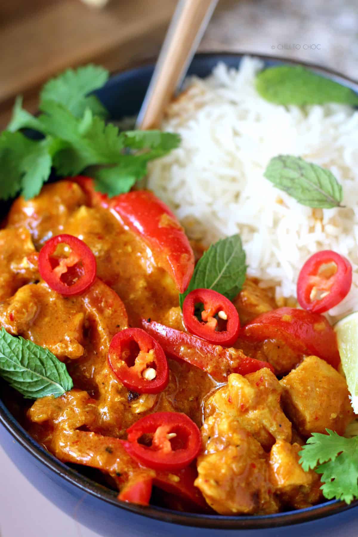 Closeup shot of Easy Thai Red Chicken Curry garnished with red chilies, coriander, mint with a side of boiled rice
