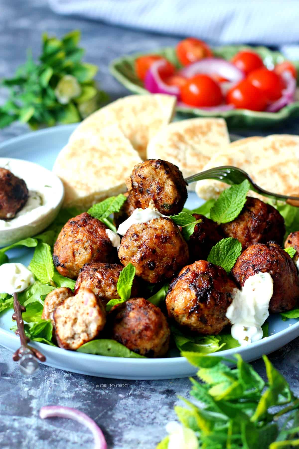 Easy Greek Meatballs (Keftedes) Meatballs on a plate with tzatziki sauce and pita bread on the side and salad behind it.