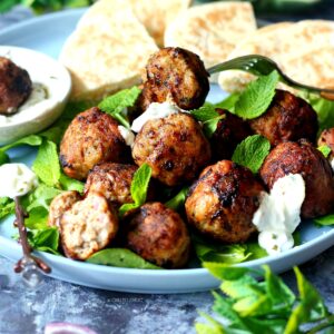 Greek meatballs (keftedes) on a plate garnished with mint and pita bread behind it