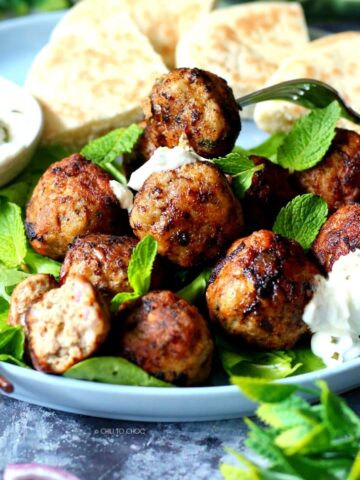 Greek meatballs (keftedes) on a plate garnished with mint and pita bread behind it