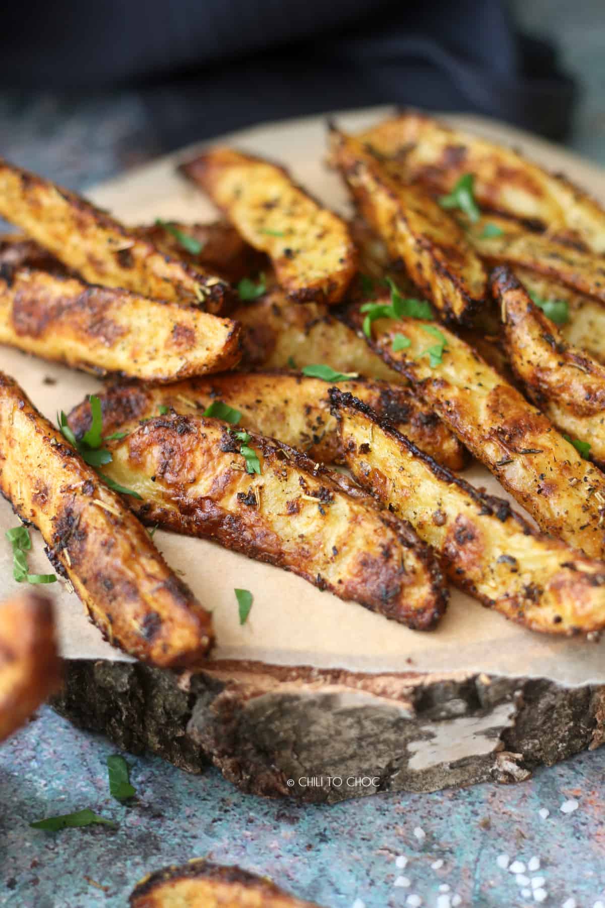 Seasoned potato wedges on a parchment paper on top of a wooden board.