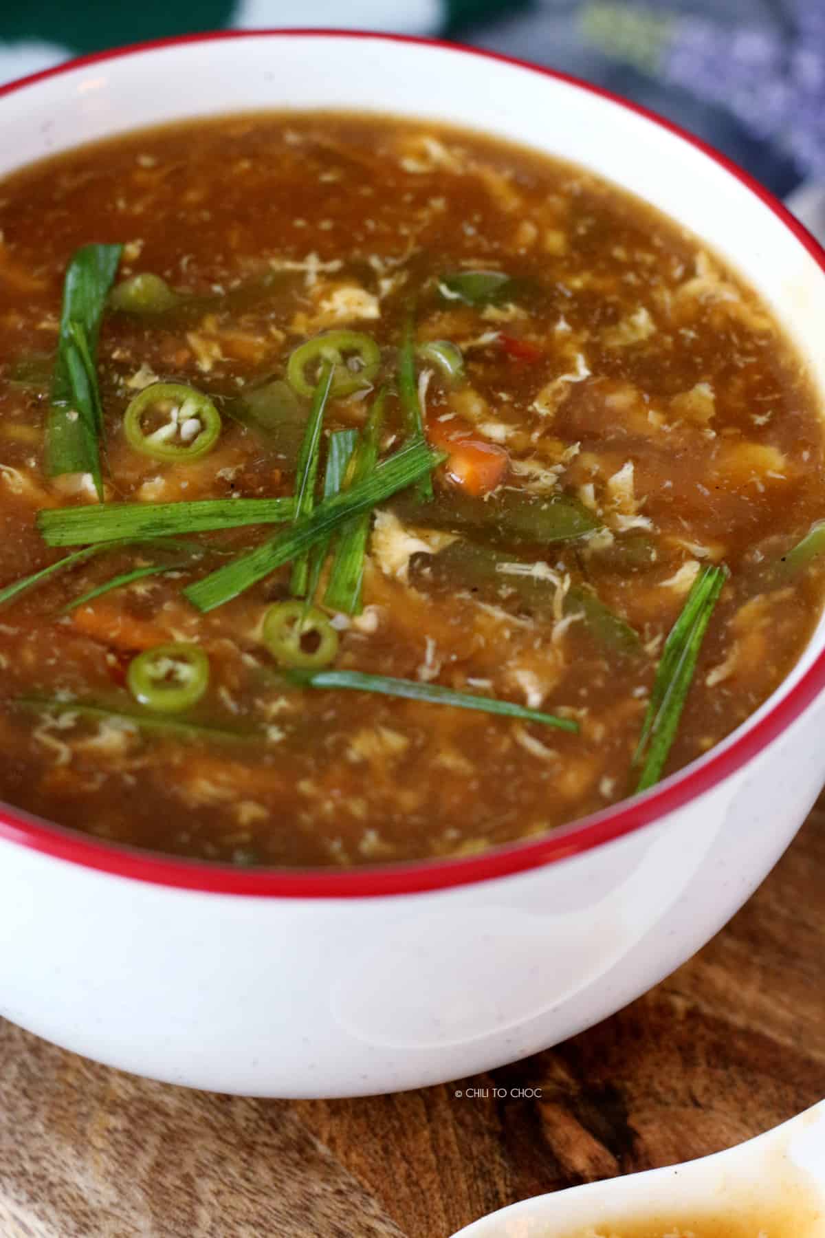 Hot and sour soup in a white bowl garnished with sliced green chili and spring onion.