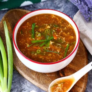 Bowl of hot and sour soup with a spoon and spring onion on the side