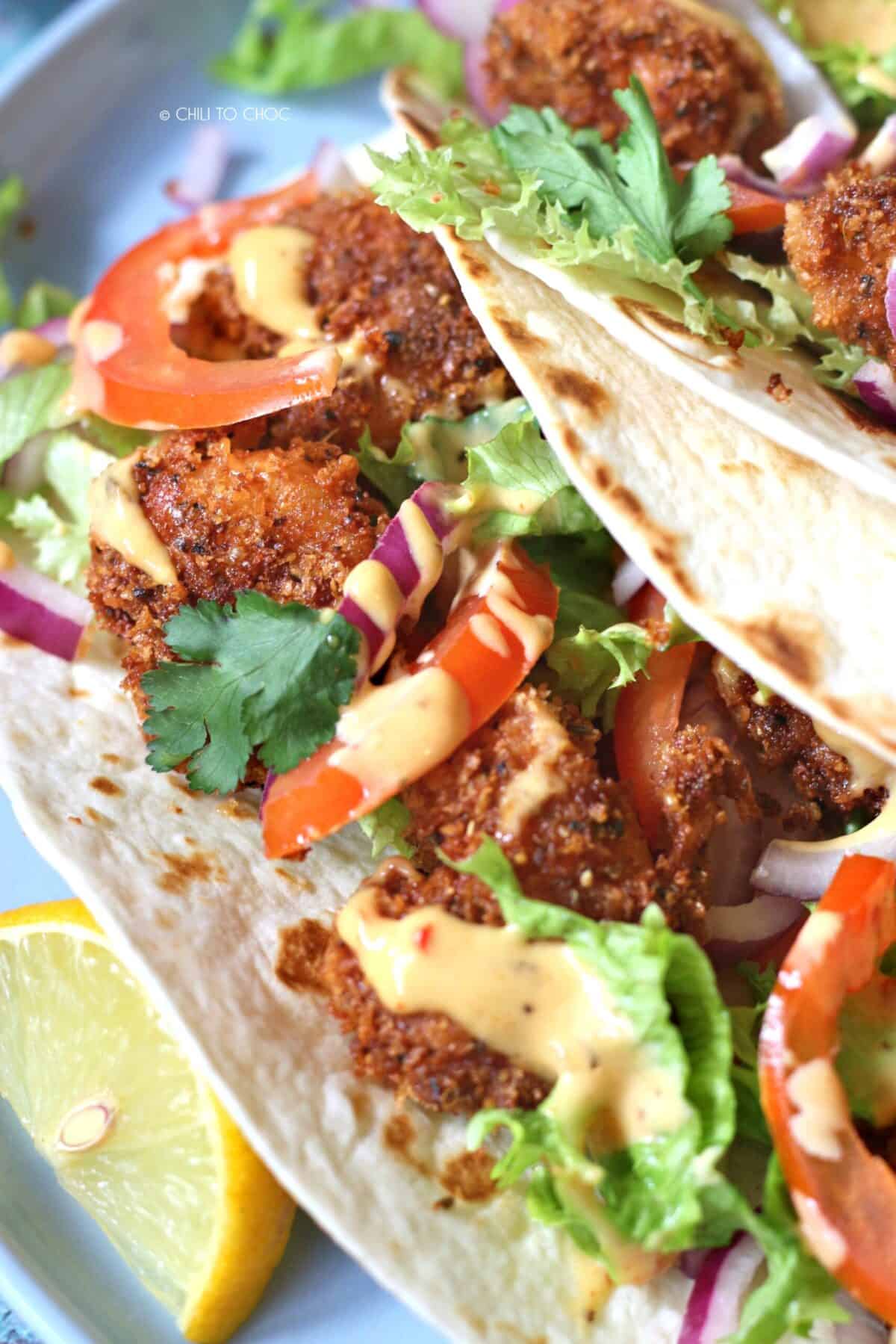 Closeup of crispy shrimp tacos with sliced onion, tomatoes, lettuce and dressing