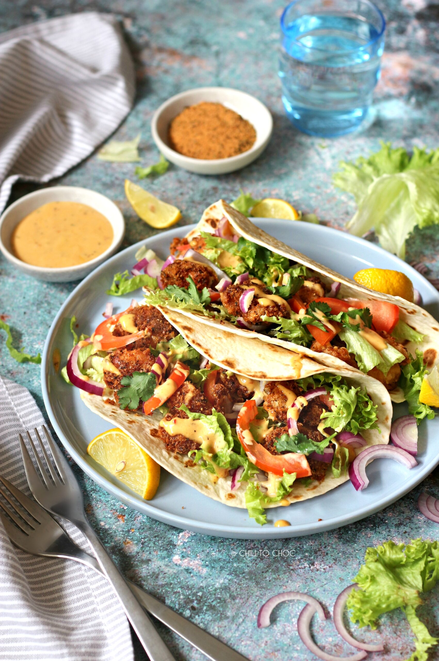 Cajun Shrimp Tacos Shrimp tacos on a blue plate with lemon wedges and different ingredients around it