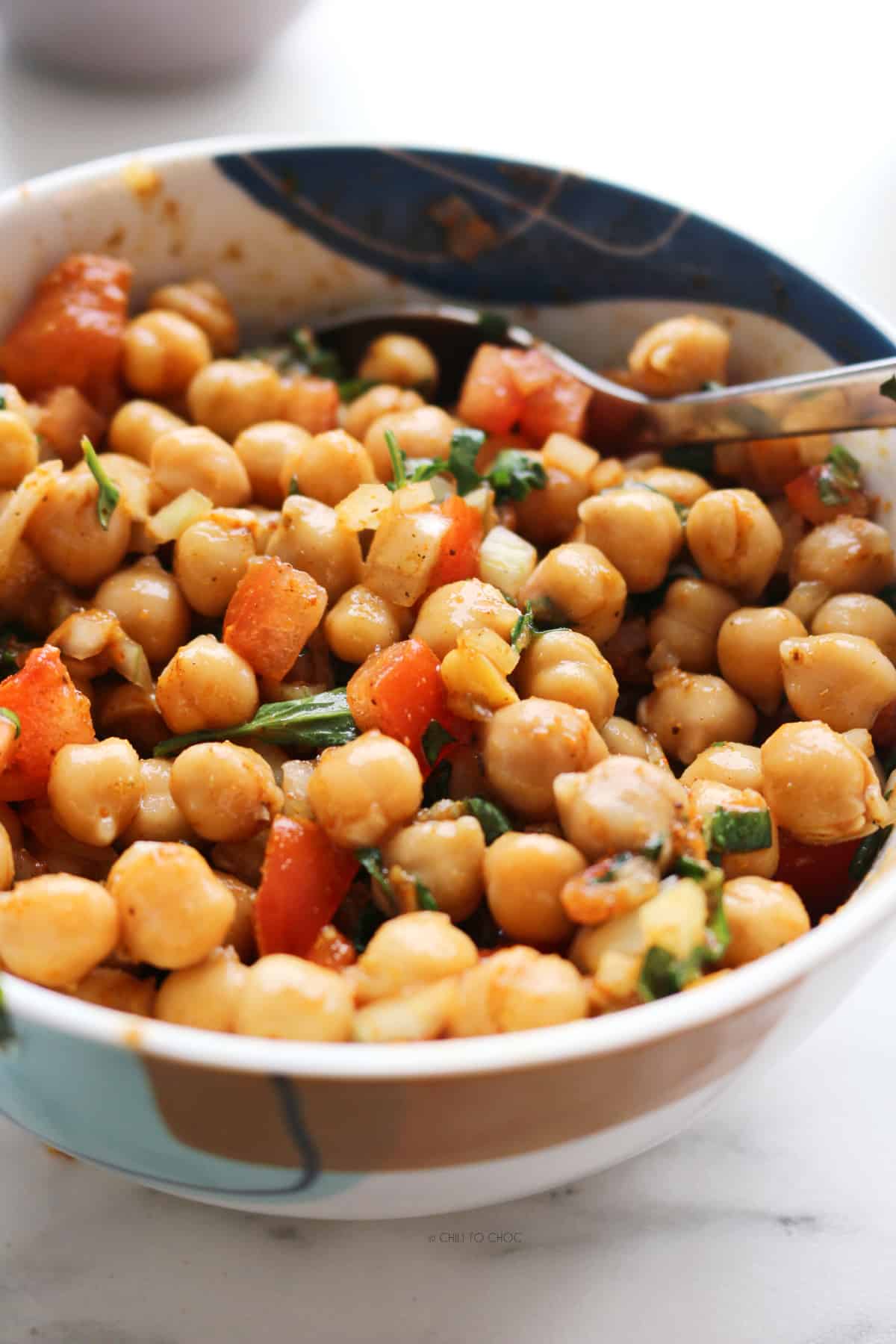 A bowl of boiled chickpeas with diced tomato and coriander with a spoon in it.