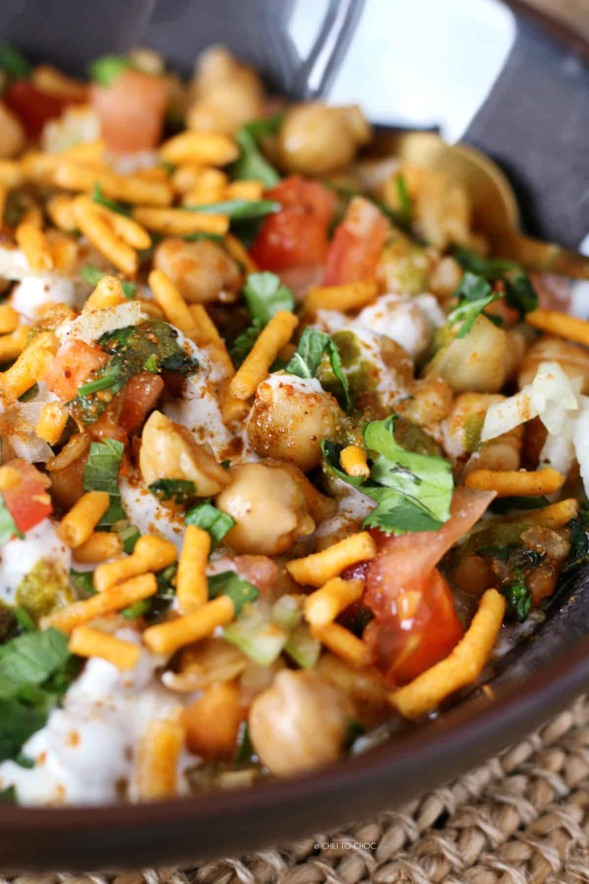 Close up of boiled chickpeas with diced tomato, sev, yogurt and fresh coriander.