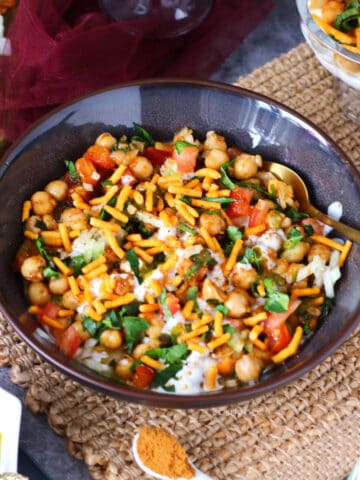 A shallow plate of channa chaat with gold spoon inside it.