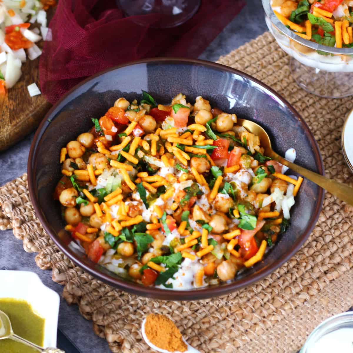 A shallow plate of channa chaat with gold spoon inside it.