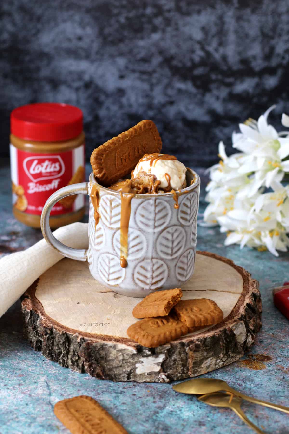 Biscoff mug cake on a wood slab with cookie spread jar in the back.