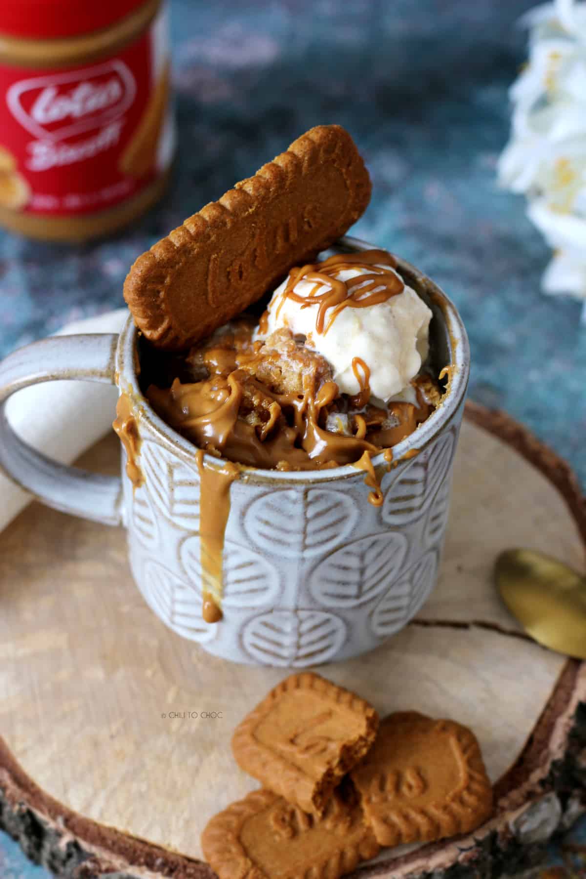 Biscoff mug cake in a grey mug with cookie and vanilla ice cream on top.