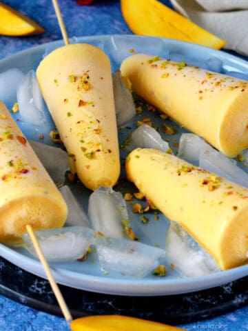 Mango Kulfis on some ice cubes garnished with chopped pistachio