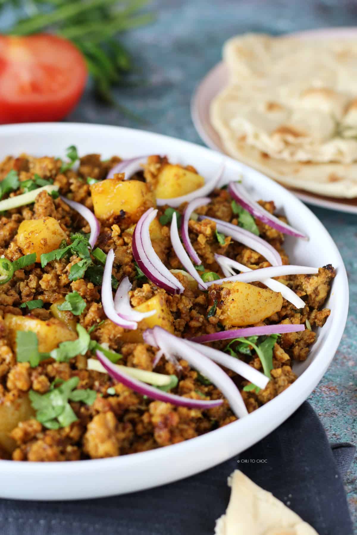 Ground Beef and Potato Curry in a dish with sliced red onion and chopped coriander leaves.