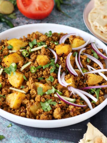 Aloo keema in a white serving dish with garnishes on top