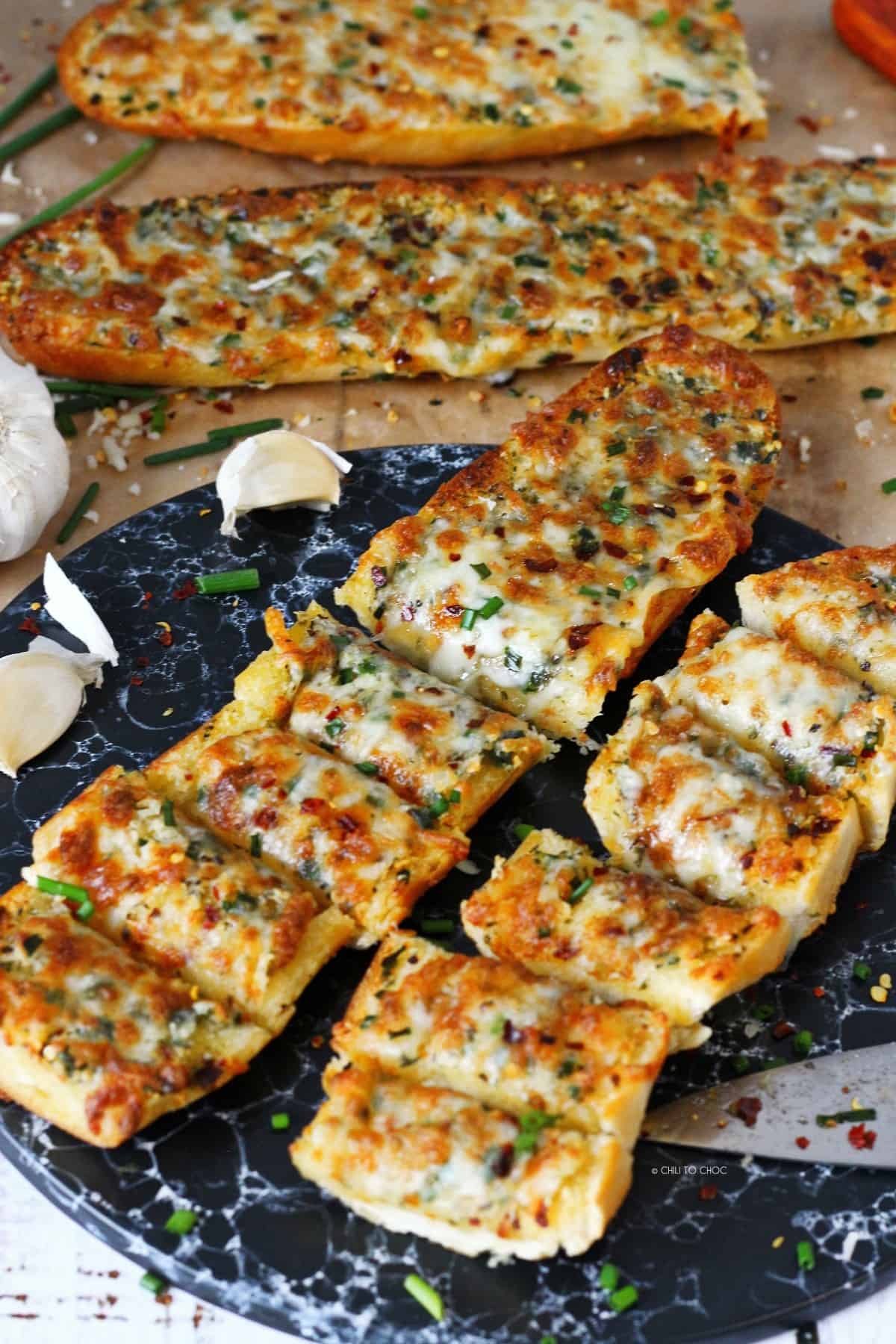 Sliced garlic bread with cheese on a black serving platter