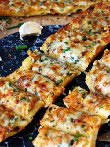 Slices of cheesy garlic bread served on a black platter with chives on top