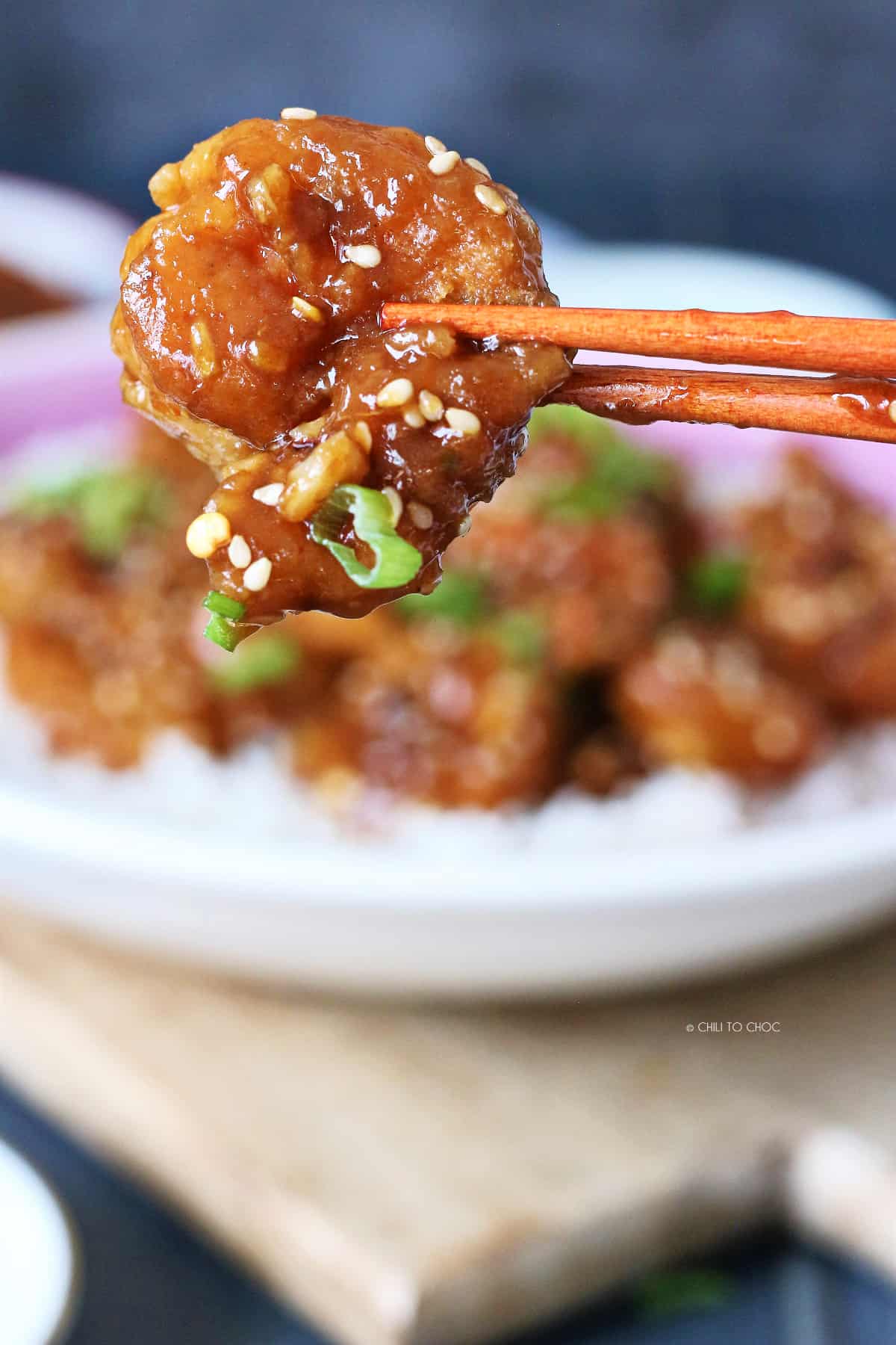A pair of chopsticks holding glazed shrimp with sesame seeds