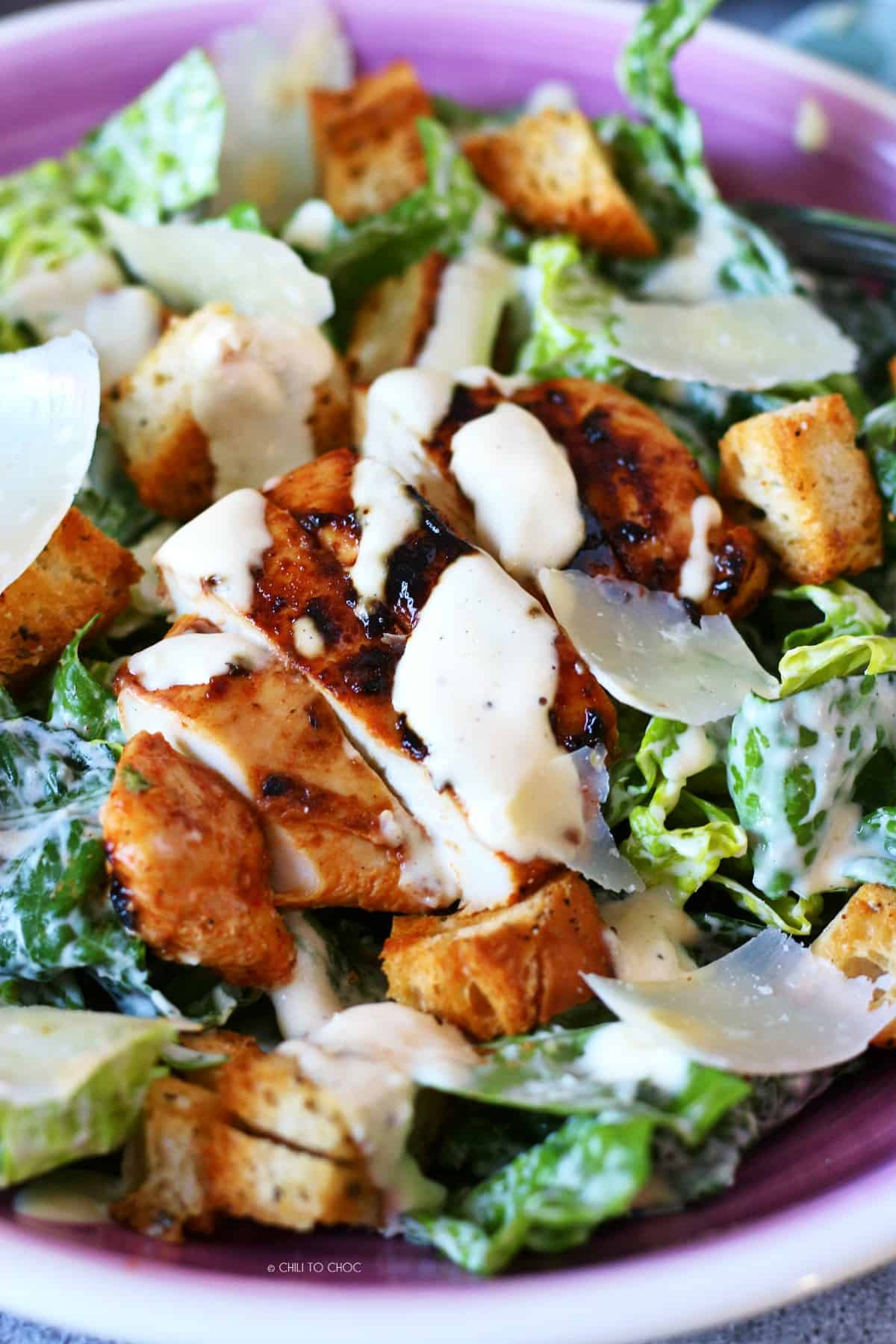 Grilled chicken slathered with Caesar dressing on top of sliced lettuce leaves.